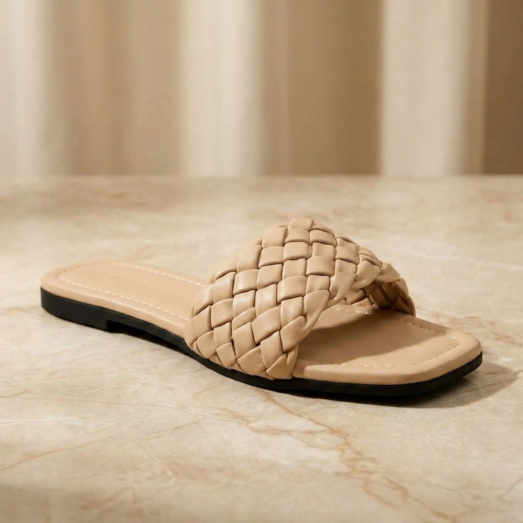 "Minimalist studio photography of a single UHR Collection women's black braided flat slide sandal, shot from a clean side profile angle on a textured beige matte surface."