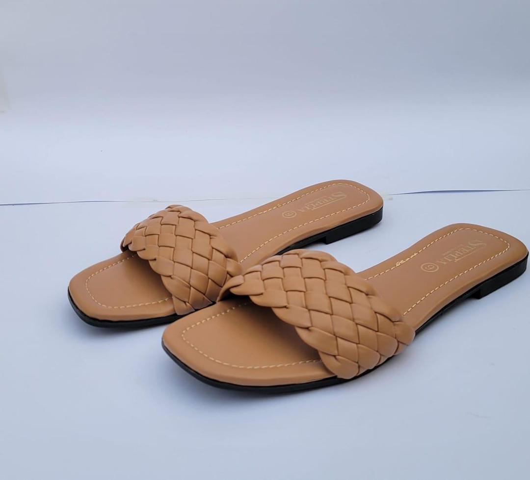 "Minimalist studio photography of a single UHR Collection women's black braided flat slide sandal, shot from a clean side profile angle on a textured beige matte surface."